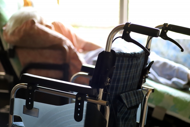 介護ベッドでリクライニングして横たわる高齢女性と車椅子