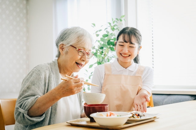 笑顔で食事する高齢女性と介護士