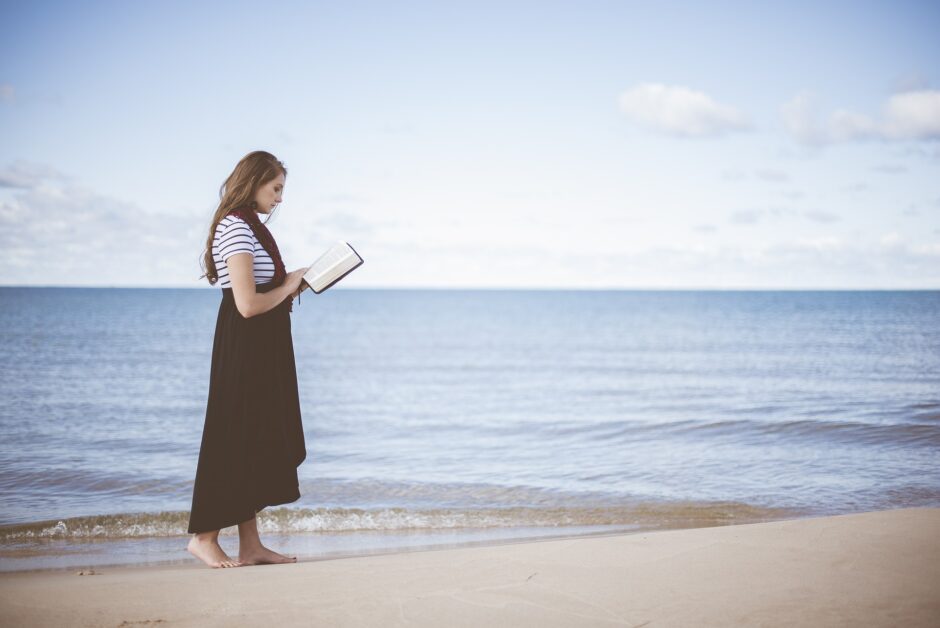 波打ち際を歩きながら読書する女性