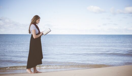 波打ち際を歩きながら読書する女性